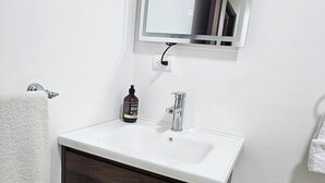 Un baño con lavamanos blanco, tocador de madera oscura, espejo y toallero.