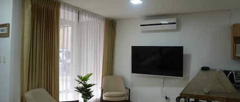 A living room with a flat-screen TV, two chairs, a small table, and a potted plant.