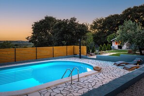 A swimming pool with a stone deck, a wooden fence, and a view of trees and a building in the background. - Villa Manda Adriatic Heated Pool (Skradin)