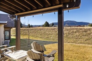 Een overdekt terras met stoelen en een tafel, met uitzicht op een grasveld en verre bergen.