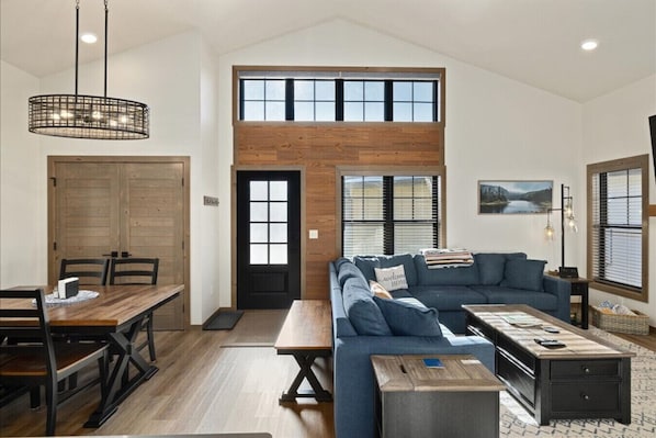 A spacious living area with a high ceiling, a wooden dining table, a blue sofa, and a wooden coffee table. - Ski Run View Red Lodge (Red Lodge)