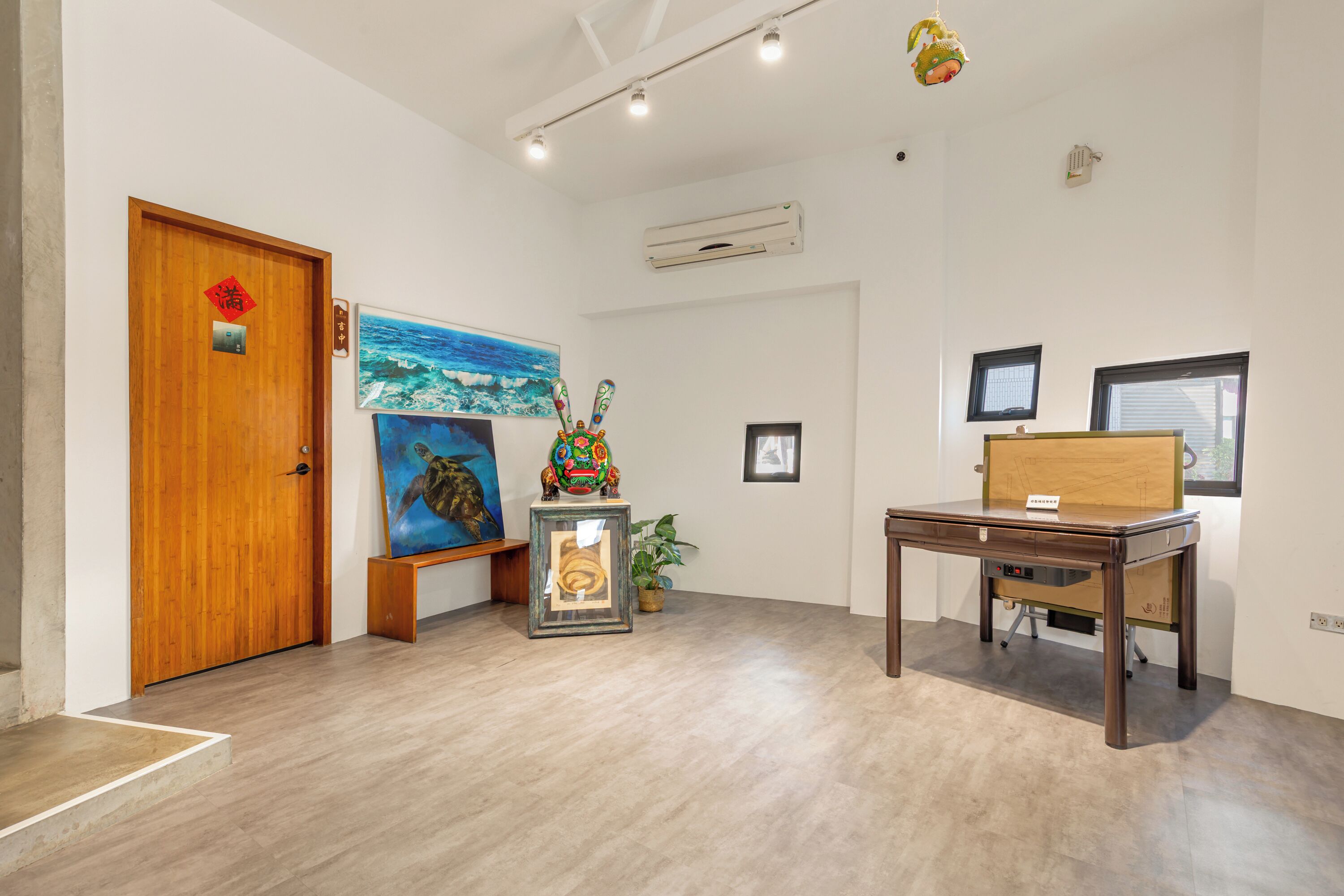 Una habitación con una puerta de madera, un cuadro enmarco, una mesita pequeña y una planta en maceta.
