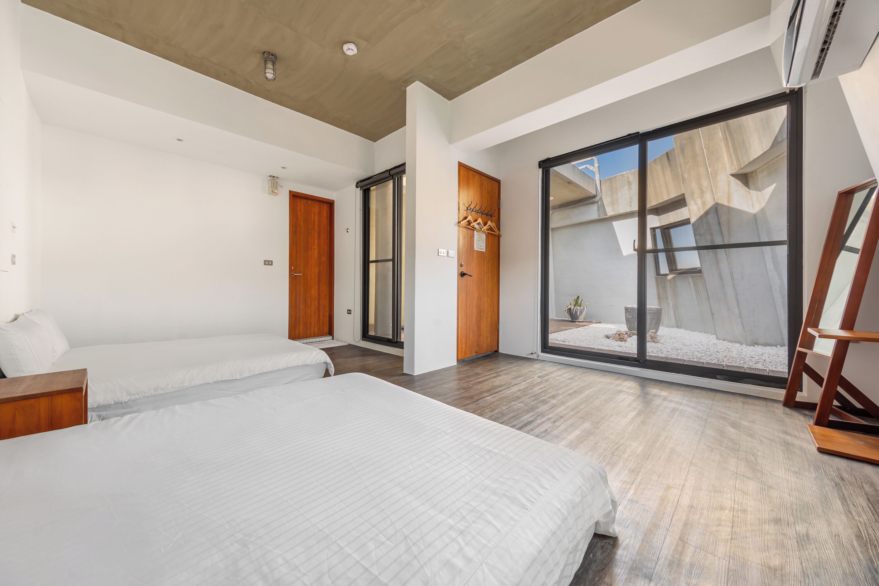 A modern hotel room with two beds, a large sliding glass door leading to a balcony, and a wooden floor.