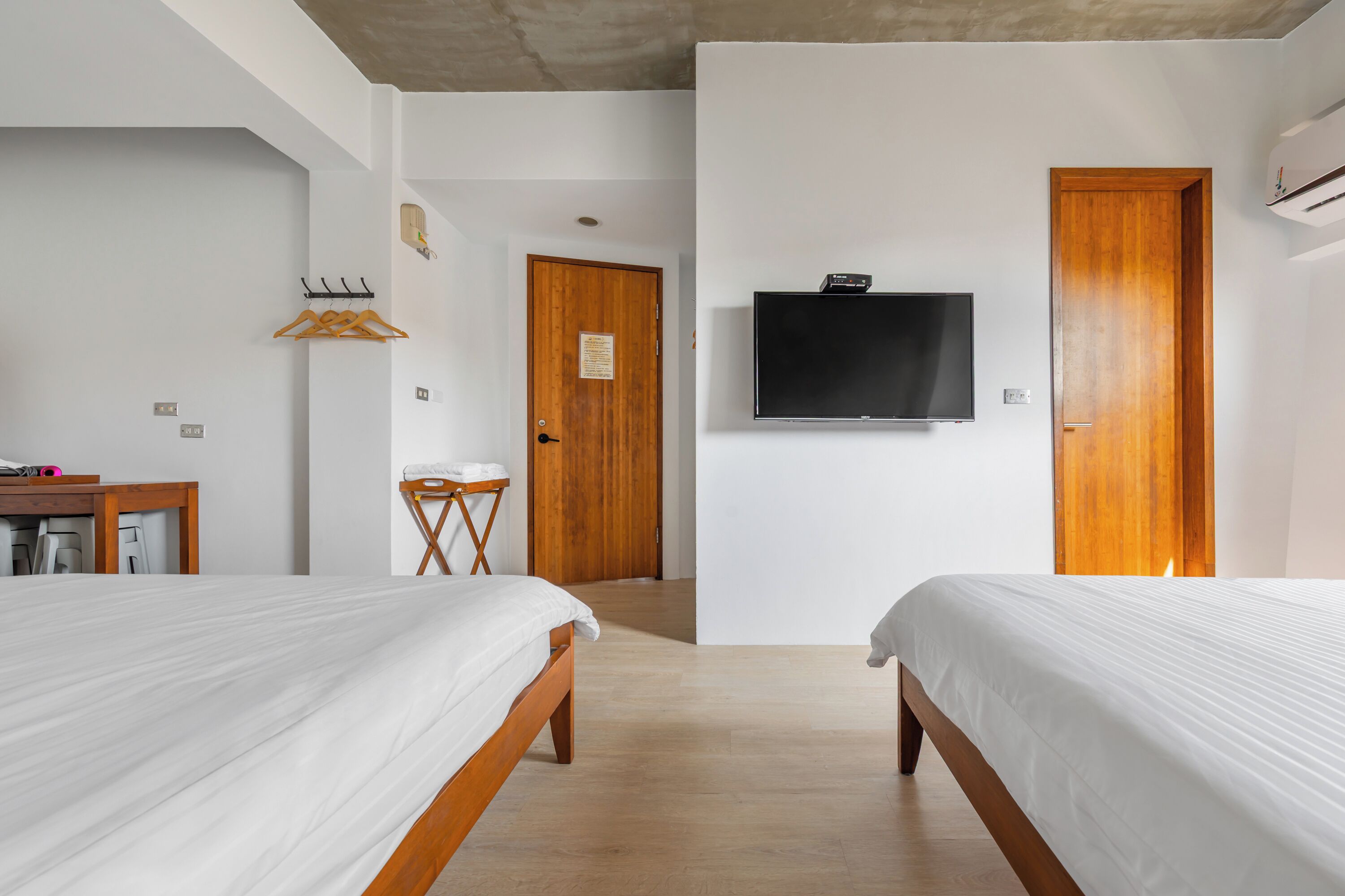 Ein Hotelzimmer mit zwei Betten, einem Fernseher, Holztüren und einem kleinen Schreibtisch mit Stuhl.