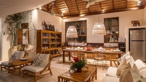 A spacious living area with a dining table, chairs, a sofa, and a kitchen in the background.