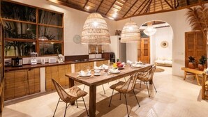 A spacious kitchen with a large dining table, wooden cabinets, and a thatched ceiling.