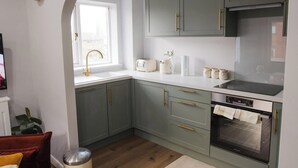A kitchen with green cabinets, a white countertop, a sink with a gold faucet, a toaster, a kettle, and an oven.