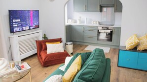 A compact living space with a sofa, a red armchair, a green sofa, a kitchen area with a stove and cabinets, and a flat-screen TV mounted on the wall.