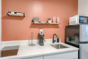 Una cocina con cubierta blanca, pileta, cafetera, microondas y refrigerador.