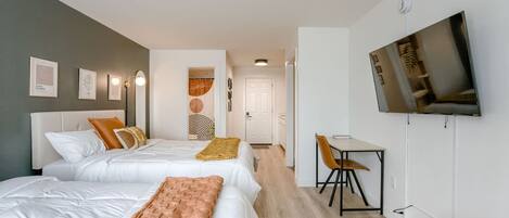 A hotel room with two beds, a desk, a chair, a television, and artwork on the walls.