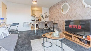Una sala de estar moderna con un televisor de pantalla plana, un comedor con sillas y una cocina al fondo.