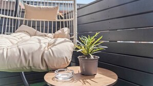 Una silla colgante con cojines, una mesita con una planta en maceta y un objeto de vidrio transparente sobre la mesa.