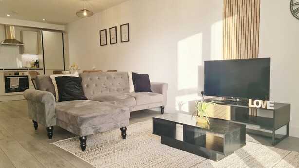 A modern living room with a grey sectional sofa, a flat-screen TV, and a coffee table.
