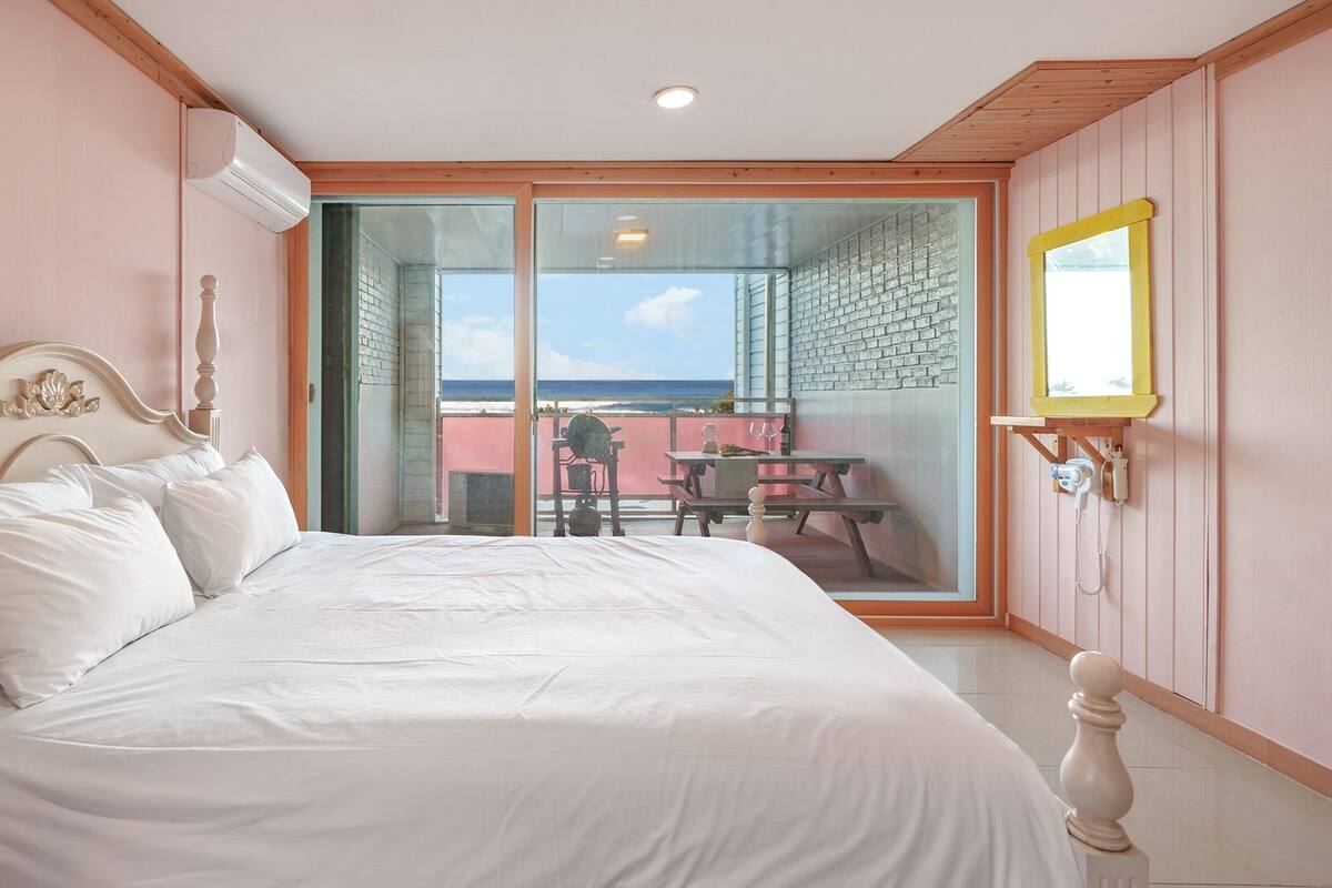 A bedroom with a bed, a window, and a view of the beach.