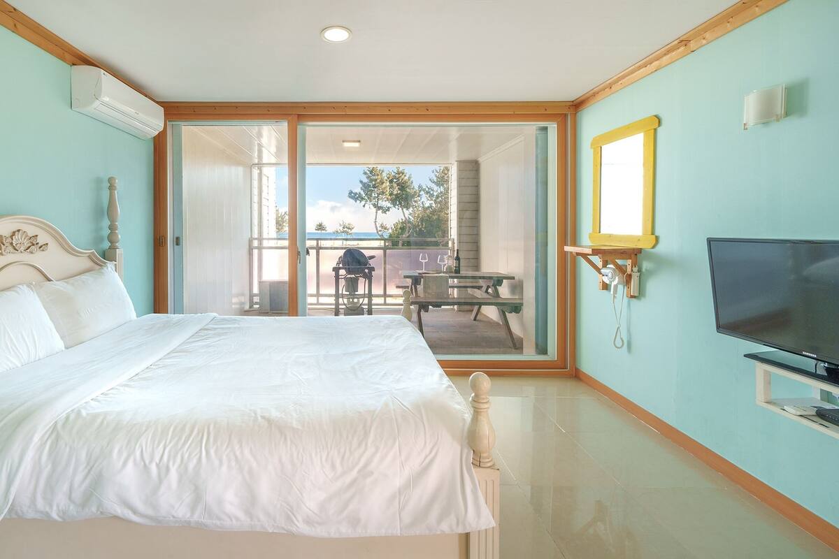 A bedroom with a bed, a television, and a sliding glass door leading to an outdoor area with a table and chairs.