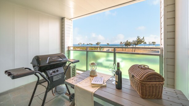 A balcony with a grill, a table with a bottle, glasses, a book, and a wicker basket. - Yangyang Bono Pet-friendly Pension (Yangyang)