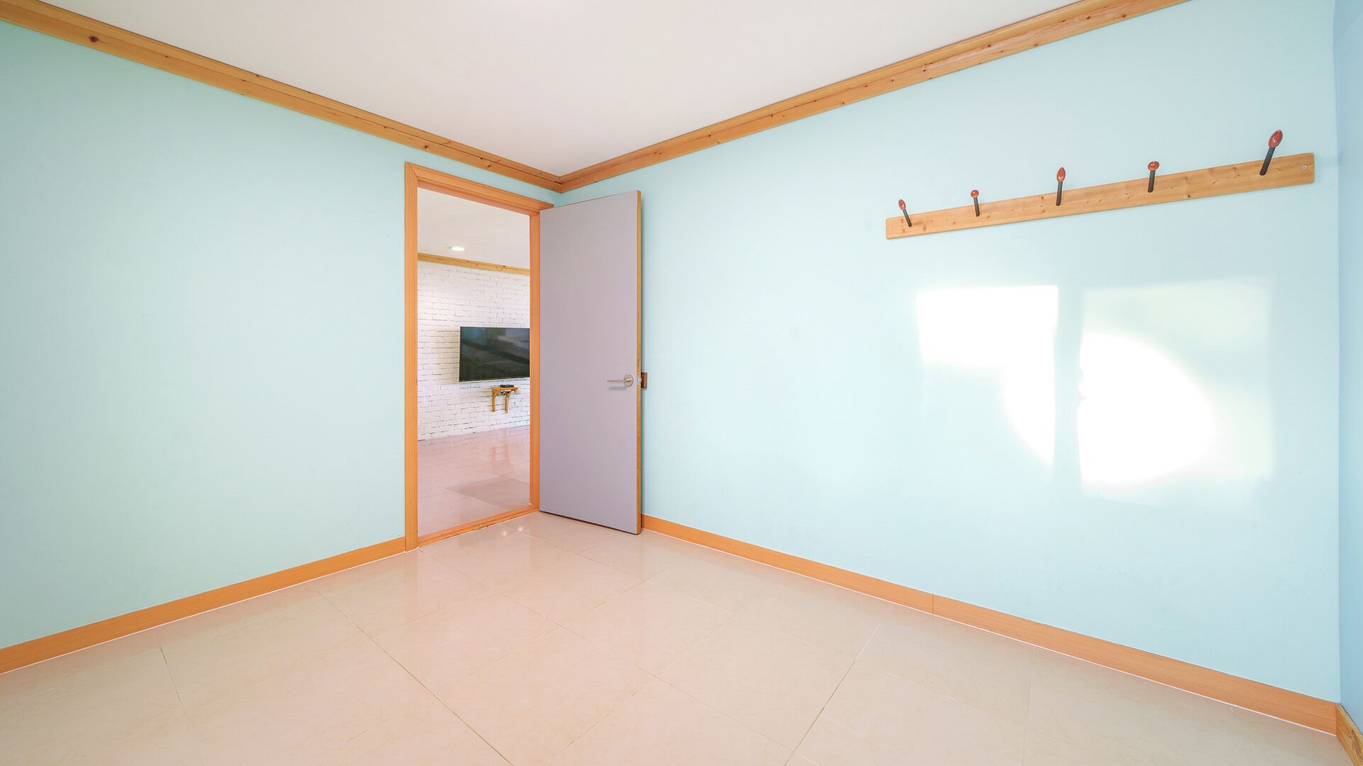 Una habitación con paredes azul claro, suelo de madera y una puerta que da a otra habitación con un televisor.