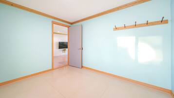Una habitación con paredes azul claro, suelo de madera y una puerta que da a otra habitación con un televisor.