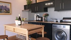 A compact kitchen with dark cabinets, a wooden table, and a built-in washing machine. - Cozy Corner Apartment (Cape Town)