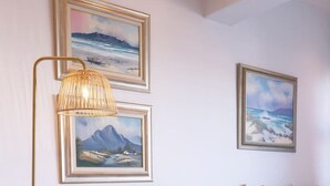 A modern living room with a beige sofa, a floor lamp, and two framed landscape paintings on the wall. - Cozy Corner Apartment (Cape Town)