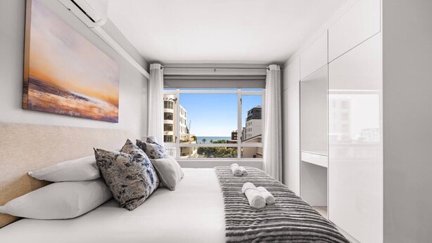 Una habitación de hotel moderna con una cama grande, vistas a la ciudad y un balcón con vista al océano.