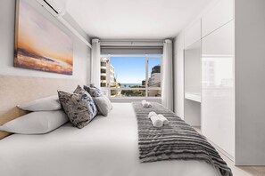 Une chambre d’hôtel moderne dotée d’un grand lit, offrant une vue sur la ville et donnant sur un balcon avec vue sur l’océan.