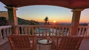 A balcony with wicker chairs and a small table, overlooking a scenic view of the sunset over a body of water and hills. - 8 Bed Villa with Private Pool & Terrace (Montouliers)