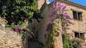 A narrow stone pathway leading to a rustic stone building with arched doorways and windows, surrounded by lush greenery and flowering plants. - 8 Bed Villa with Private Pool & Terrace (Montouliers)