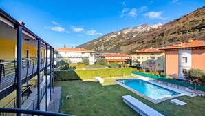 A residential building with a swimming pool, a grassy yard, and a mountain backdrop. - Torbolino - Apt with Balcony. Pool & Views, Torbole sul Garda, Italy (Torbole sul Garda)