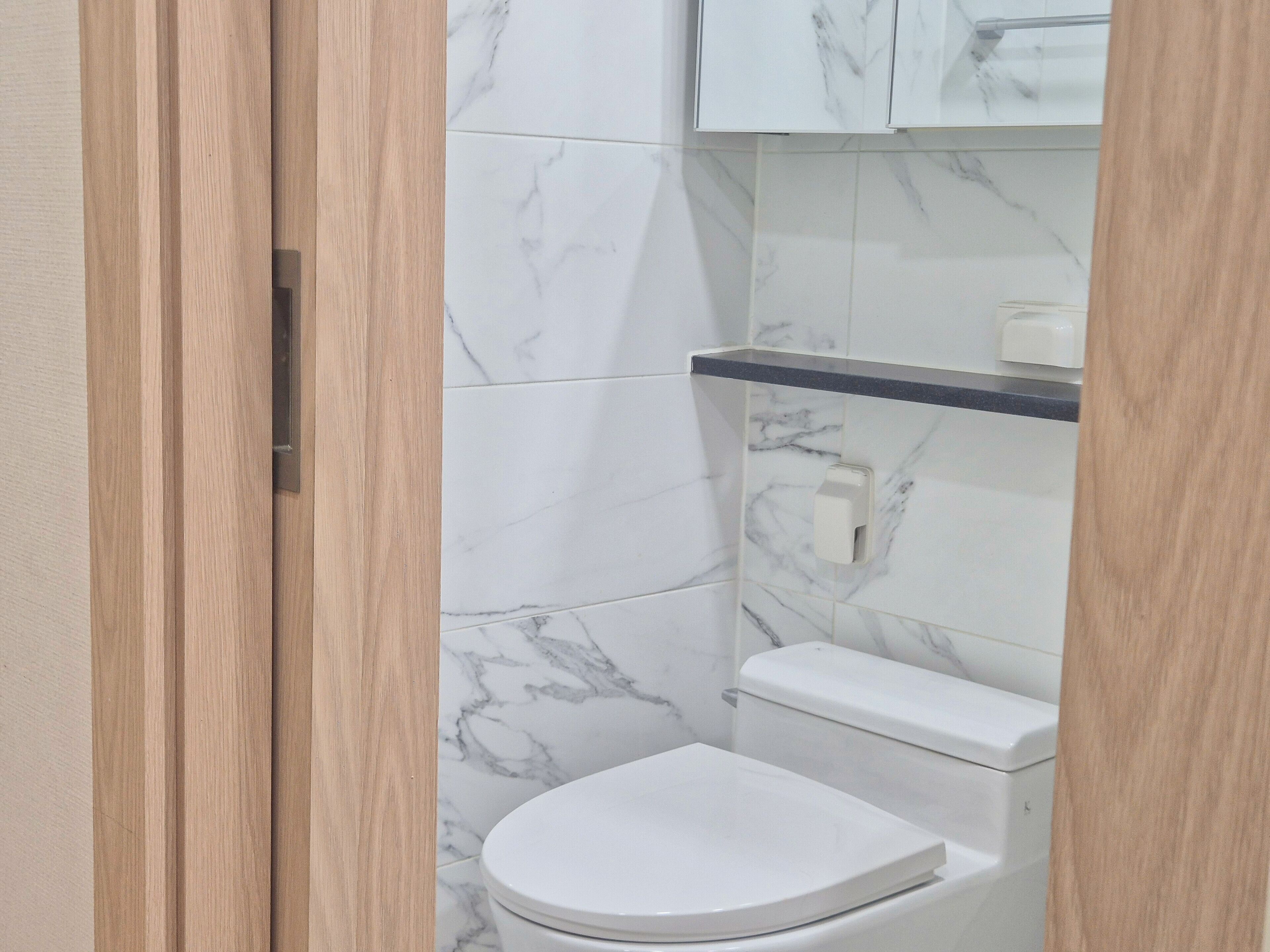 A bathroom with a toilet, a marble-tiled wall, and a wooden door.