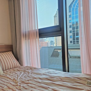 Ein Hotelzimmer mit Bett, Fenster mit Vorhängen und Blick auf Gebäude.