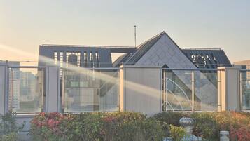 A modern building with a glass facade, a metal roof, and a garden area with shrubs and a decorative fountain.