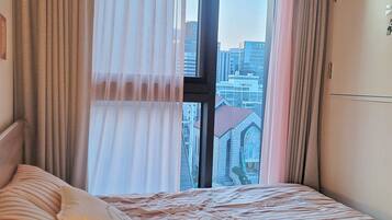 A hotel room with a large window, a bed with striped bedding, and a view of a cityscape.