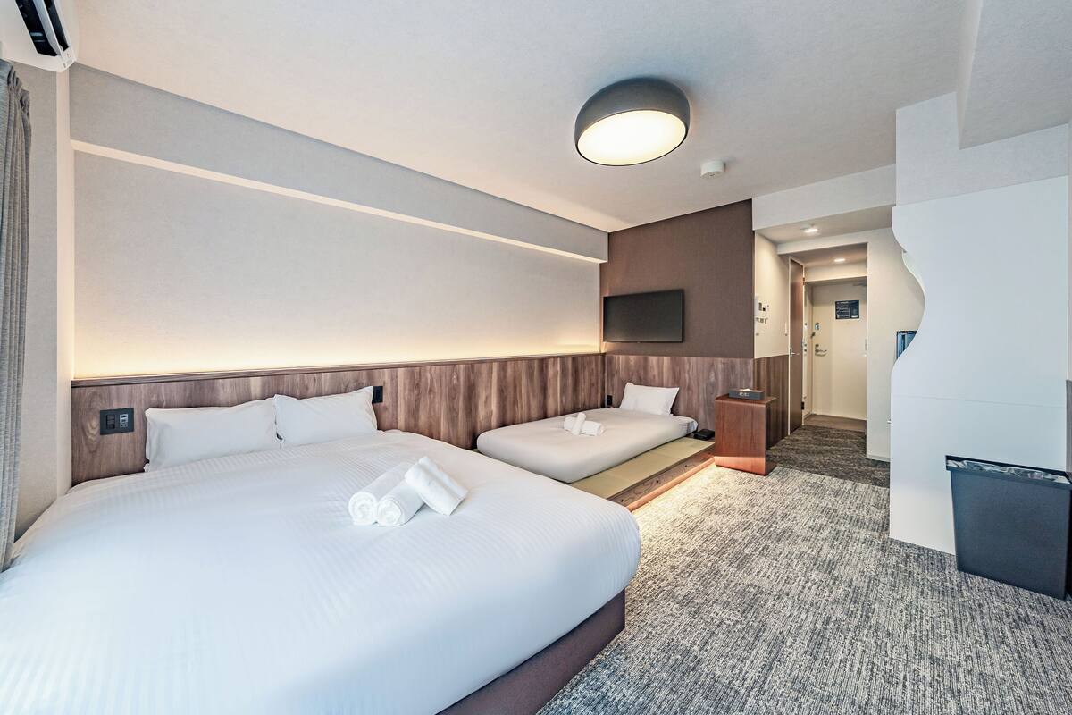 Habitación de hotel con dos camas, un televisor de pantalla plana, un cesto de basura y piso alfombrado.