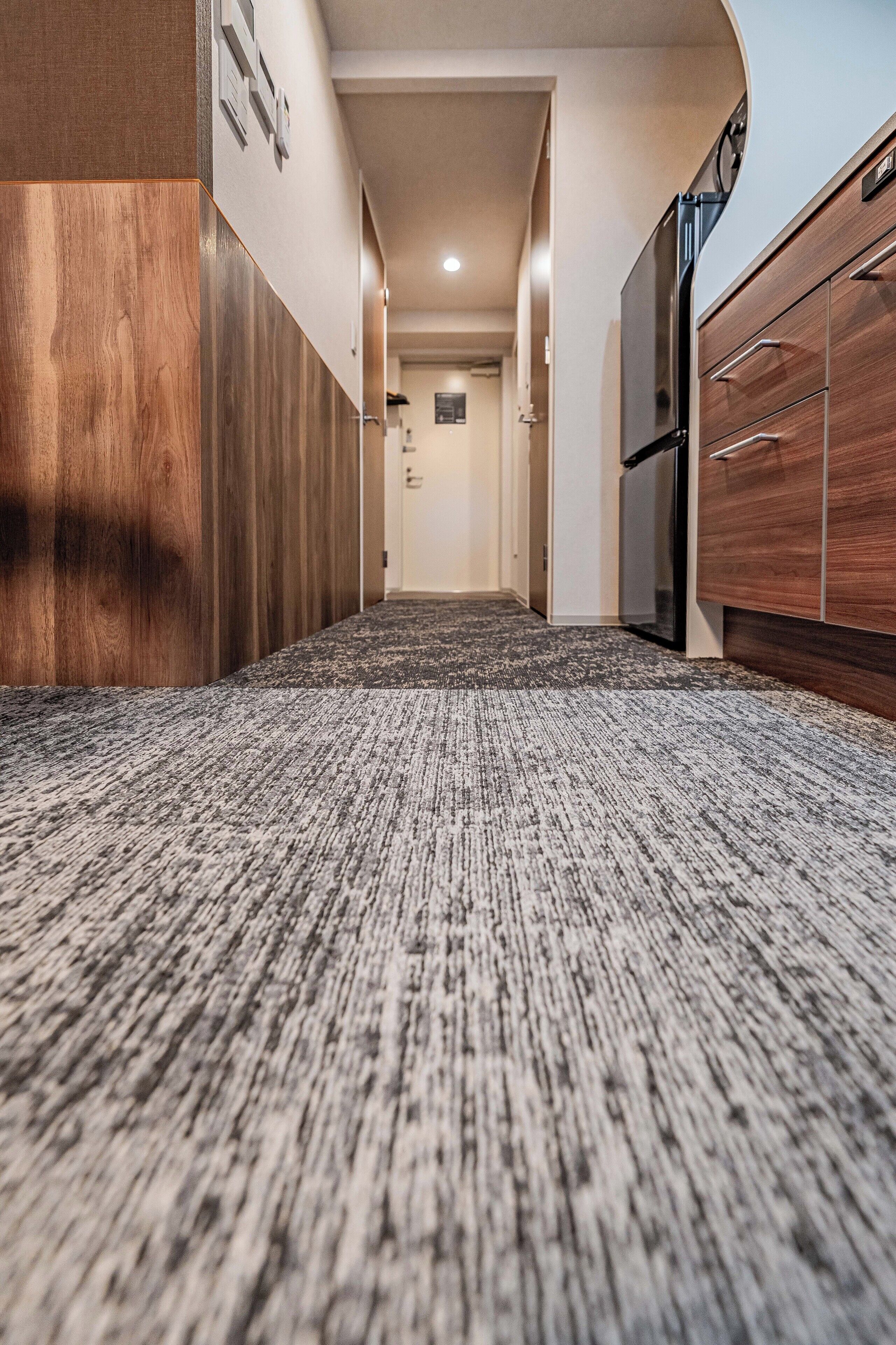 A hallway with a carpeted floor, wooden cabinets, and a refrigerator.
