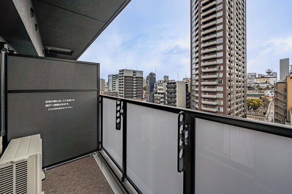 Uma varanda com vista para a cidade, com um edifício alto e outros edifícios residenciais.