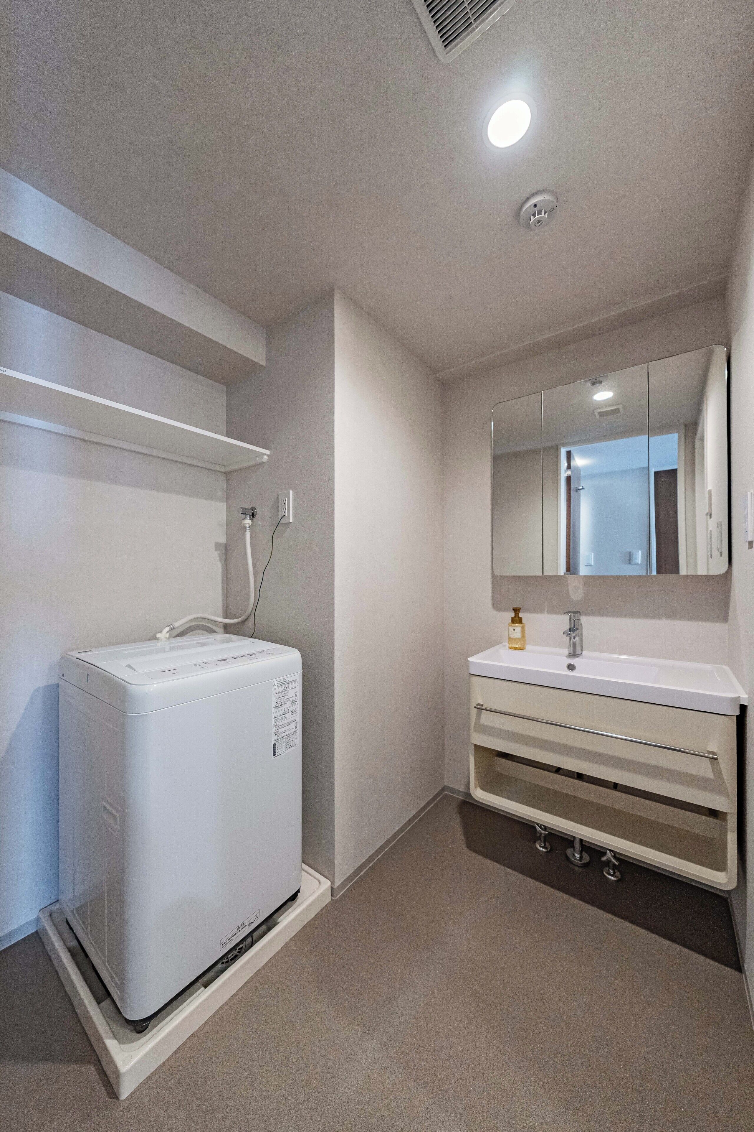 A bathroom with a white washing machine, a sink, a mirror, and a shelf.