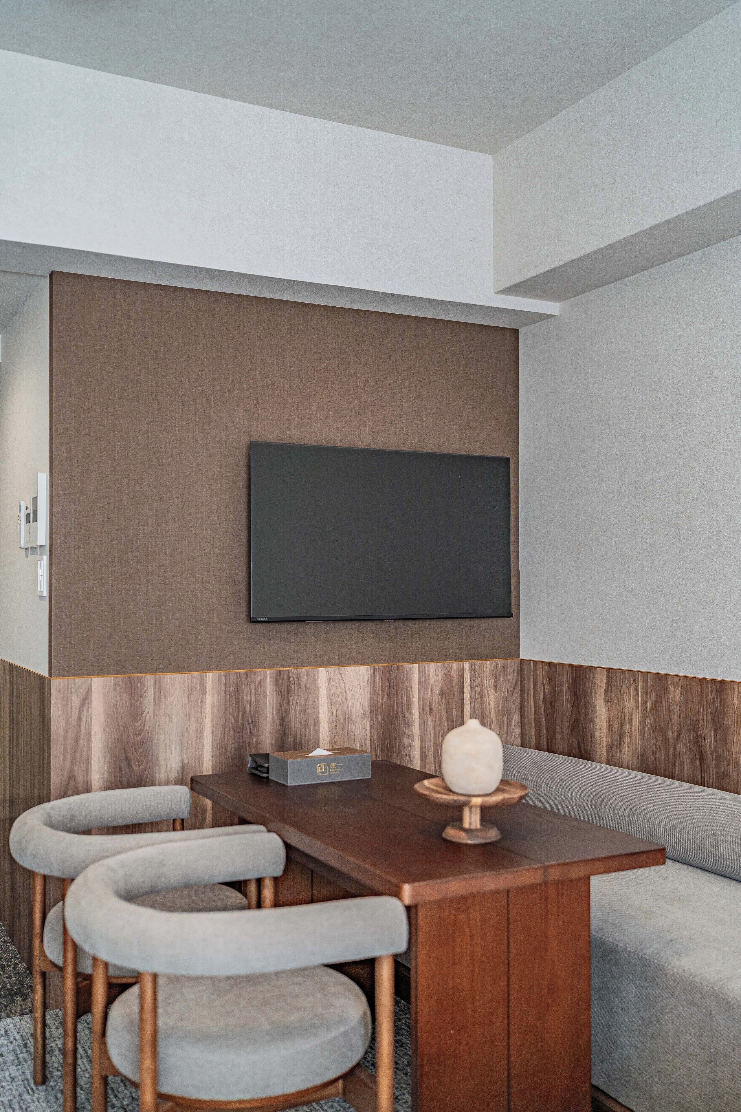 A modern interior with a wooden table, grey upholstered chairs, a flat-screen TV mounted on a wall, and a grey sofa.