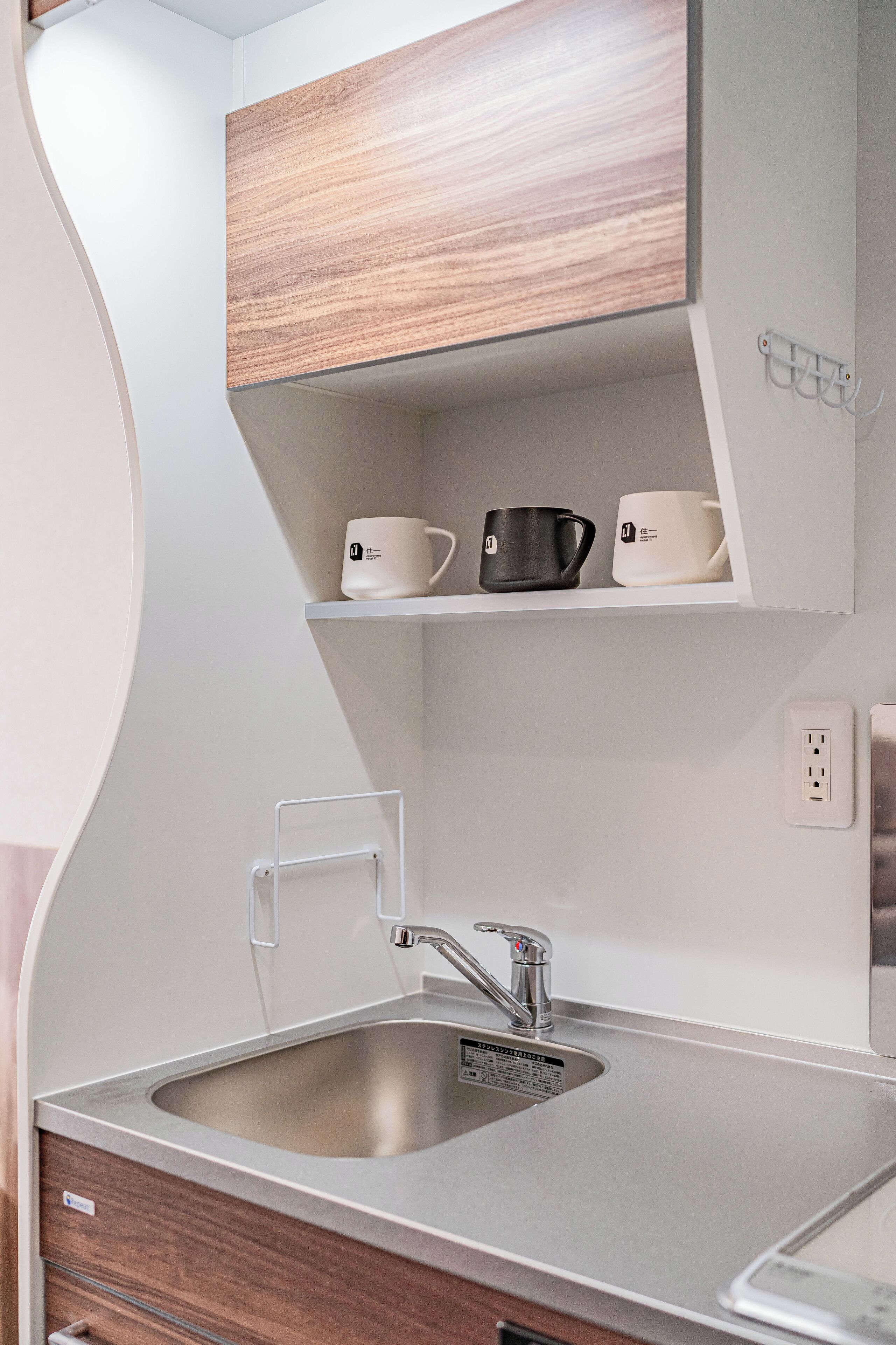 A modern kitchen with a stainless steel sink, wooden cabinets, and a built-in shelf with cups.