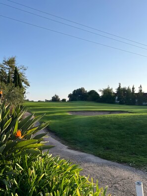 Un parcours de golf avec un ciel dégagé, un chemin de gravier et de l’herbe verte.