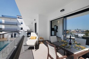 Un balcon moderne avec une piscine, un coin repas comprenant des chaises et une table dressée pour deux personnes, et une vue sur la ville à travers de grandes fenêtres.