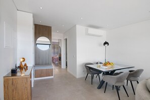 Un espace repas moderne avec une table en verre, des chaises grises et un saladier rempli de fruits.