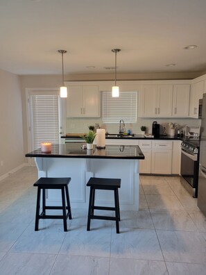 A modern kitchen with white cabinets, a black countertop, two black stools, and a stainless steel refrigerator. - Charming 2-bedroom apartment with WiFi, AC, and ADT Security in quaint Mission! (Mission)
