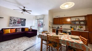 Una sala moderna con un sofá, una mesa de comedor para dos personas y una cocina con armarios de madera.