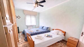 Un dormitorio con dos camas, un ventilador de techo, una ventana con cortinas y suelo de baldosas.