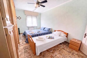 A bedroom with two beds, a ceiling fan, a window with curtains, and a tiled floor. - La Pietra sul Mare Apartment with Terrace, Pietra Ligure, Italy (Pietra Ligure)