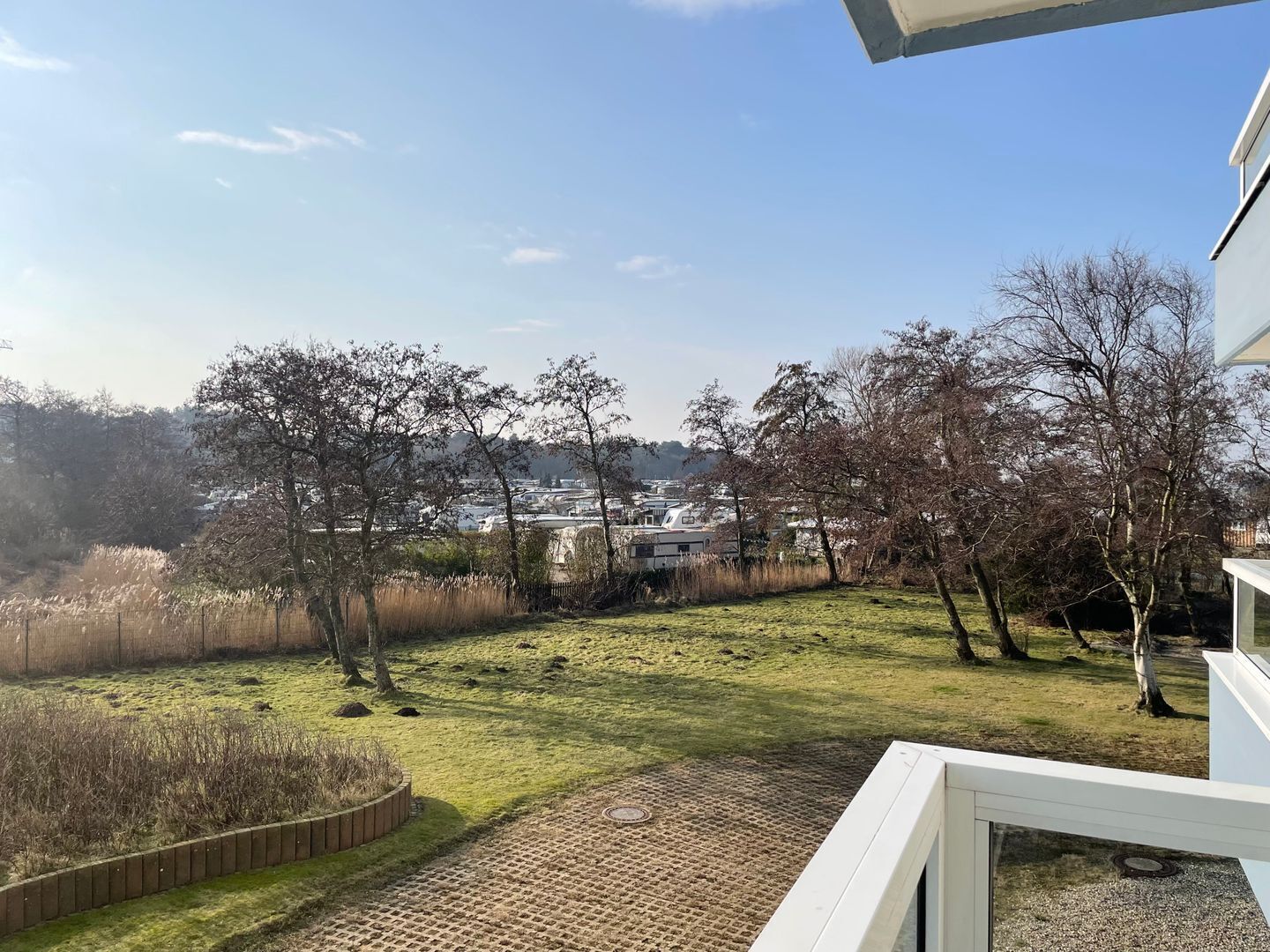 A view from a balcony overlooking a grassy yard with trees and a distant town.