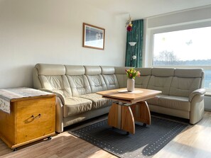 En moderne stue med en beige lædersofa, et træsofabord og et lille træskab.