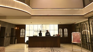 Et hotellets receptionområde med et moderne design, med en reception, en lysekrone og et stort vindue med hotellets navn.