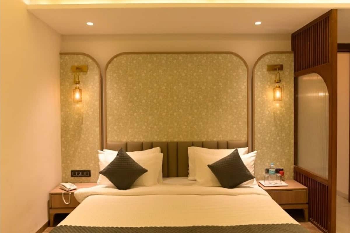 A hotel room with a large bed, two bedside tables, a nightstand, and a wall-mounted light fixture.